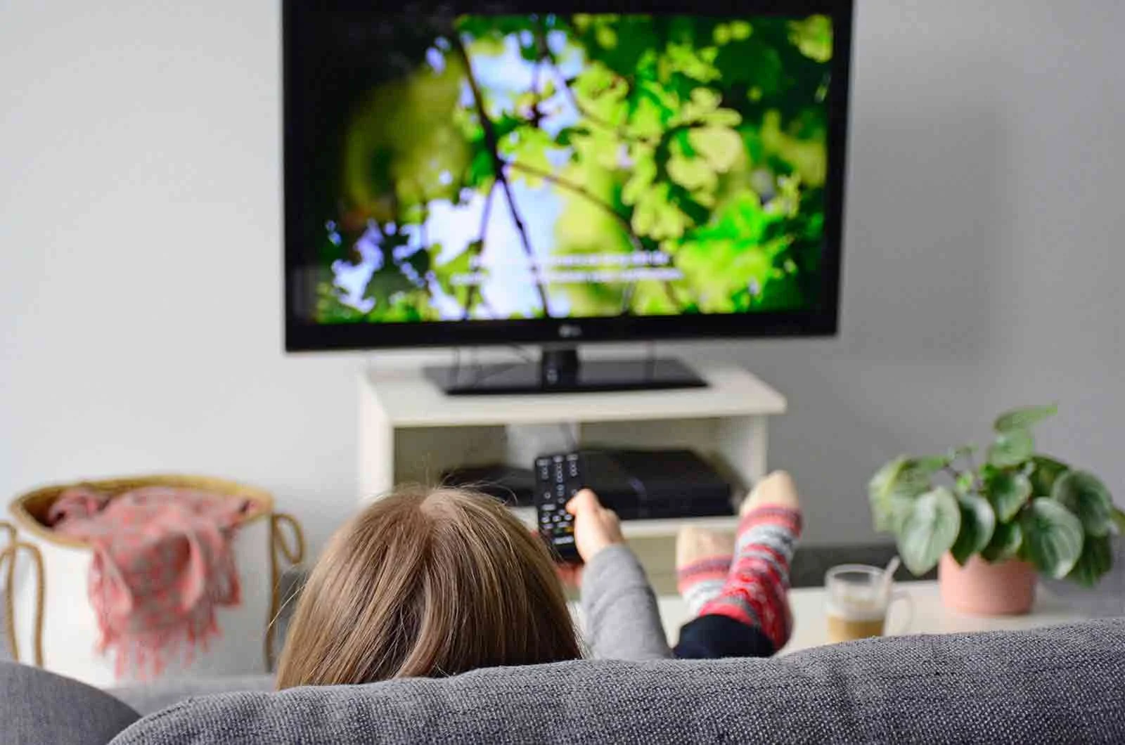 A girl sitting comfortably on the sofa at home and watching movies on TV. Concept of subtitling services for movies and else by professional subtitling companies.