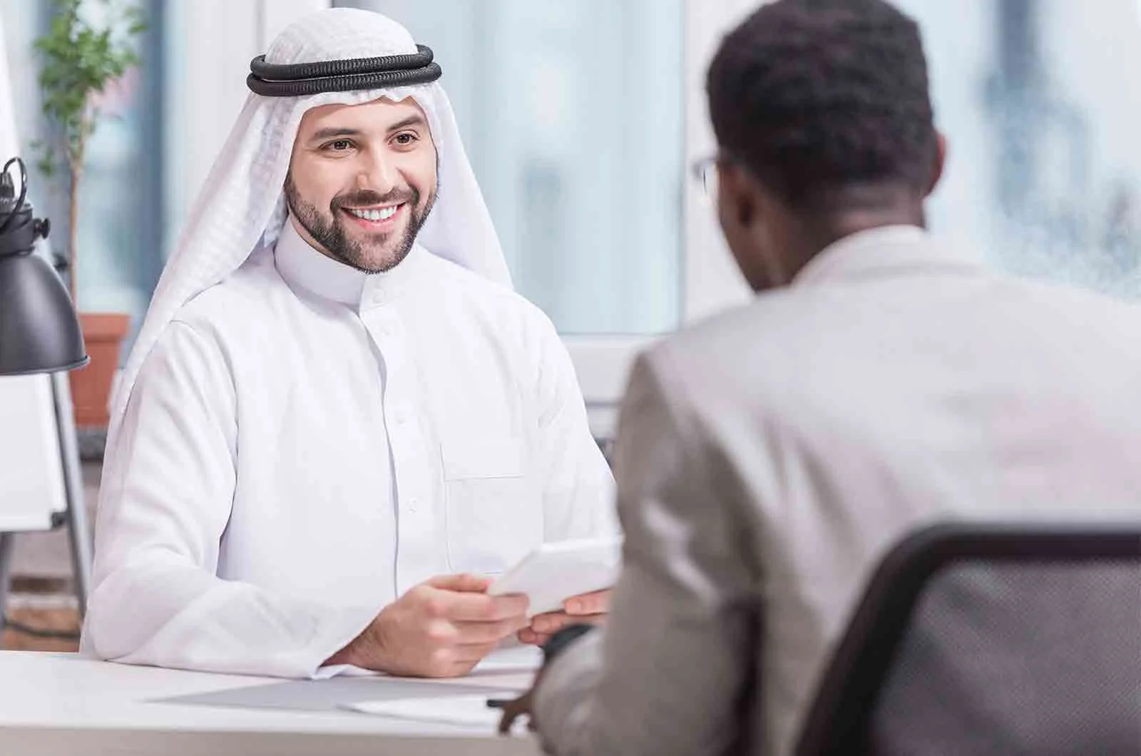 An Arabic man smiling at the man sitting in front of him. Concept of Arabic translation services.