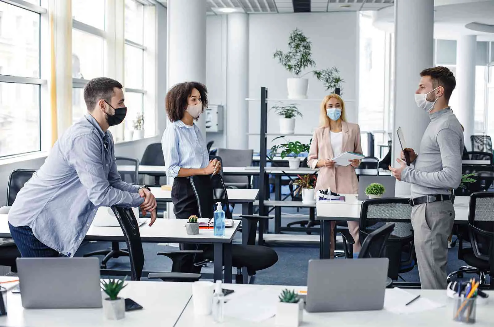 Two men and two women standing in office and wearing masks. 