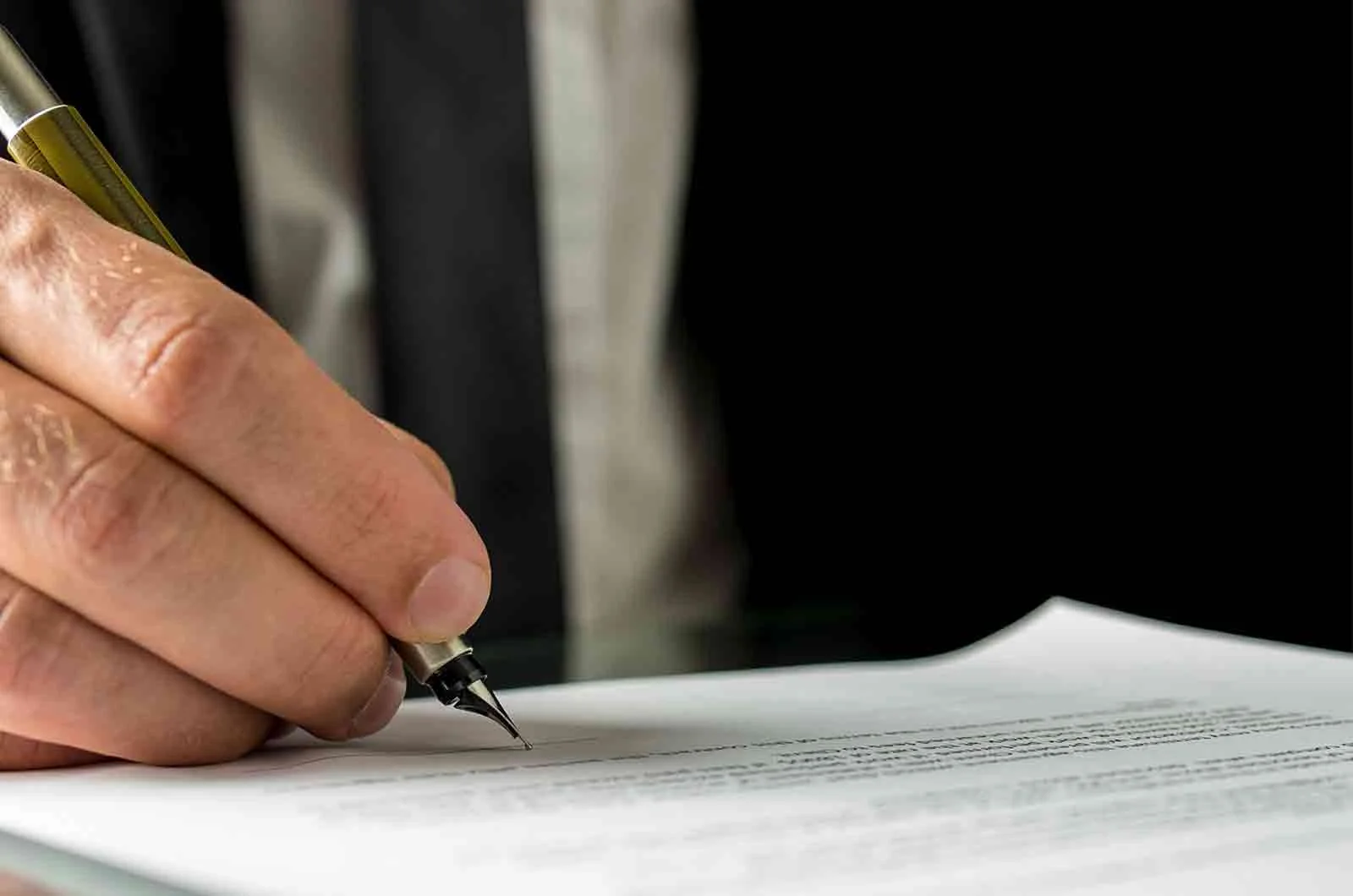 A businessman wearing a formal suit, signs papers in the company. Concept of certified translation services and UK translators.