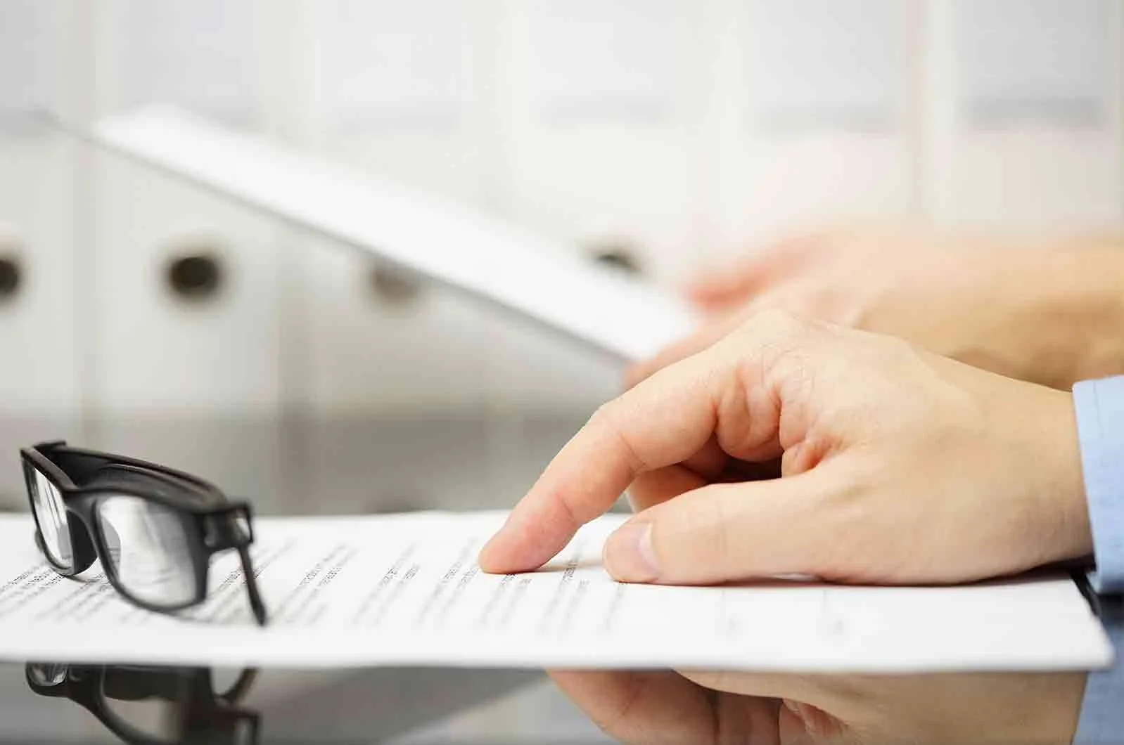 A hand pointing the finder to a paper with glasses on table.