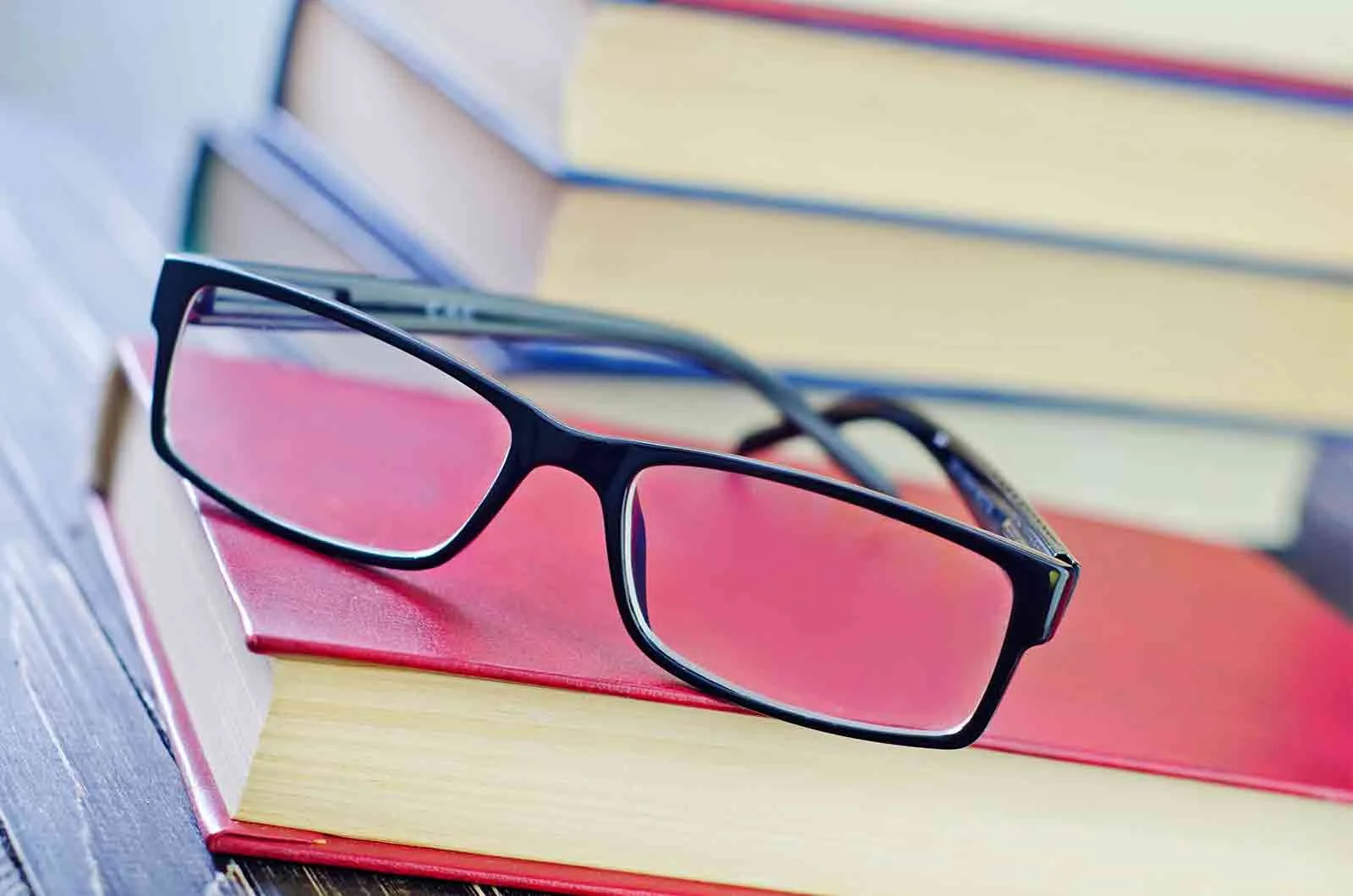 Medical glasses placed on a red book, next to several other books. Concept of editing and proofreading services and professional editors and proofreaders.