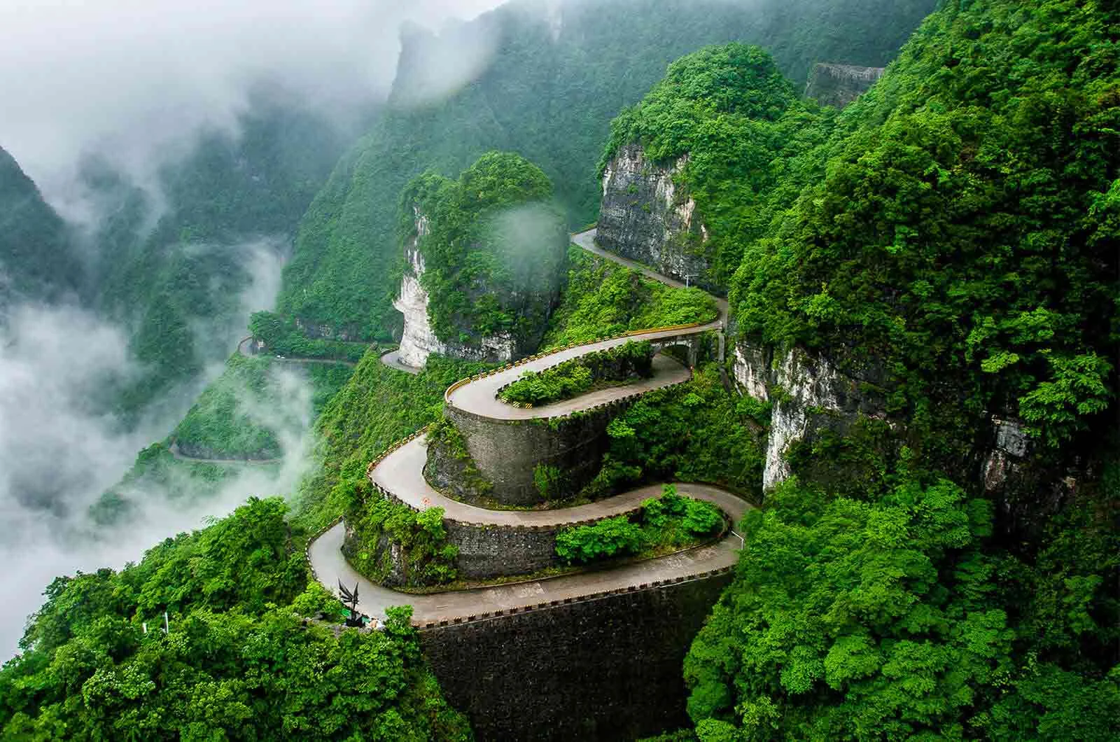 Winding road between mountains and trees in mist clouds, Hunan Province, China. Concept of Chinese translation services. 