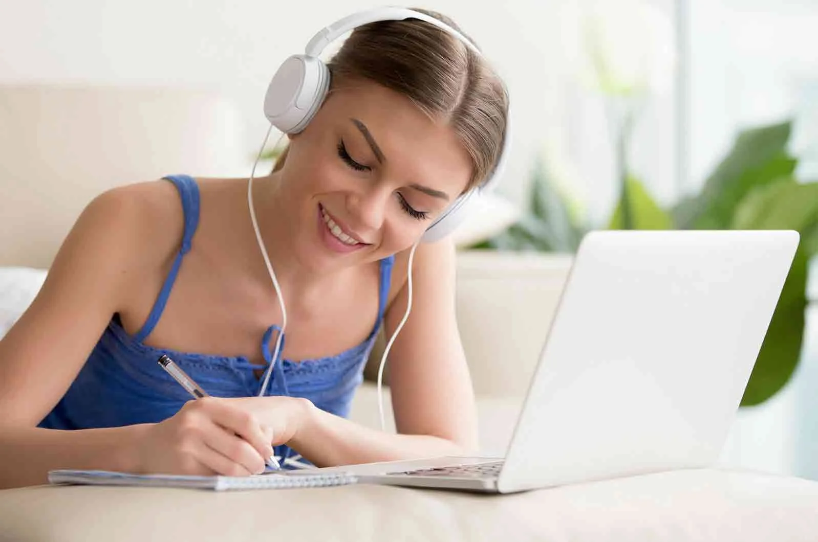 Girl with headphones writing on a notebook, with a laptop. Concept of learning languages.
