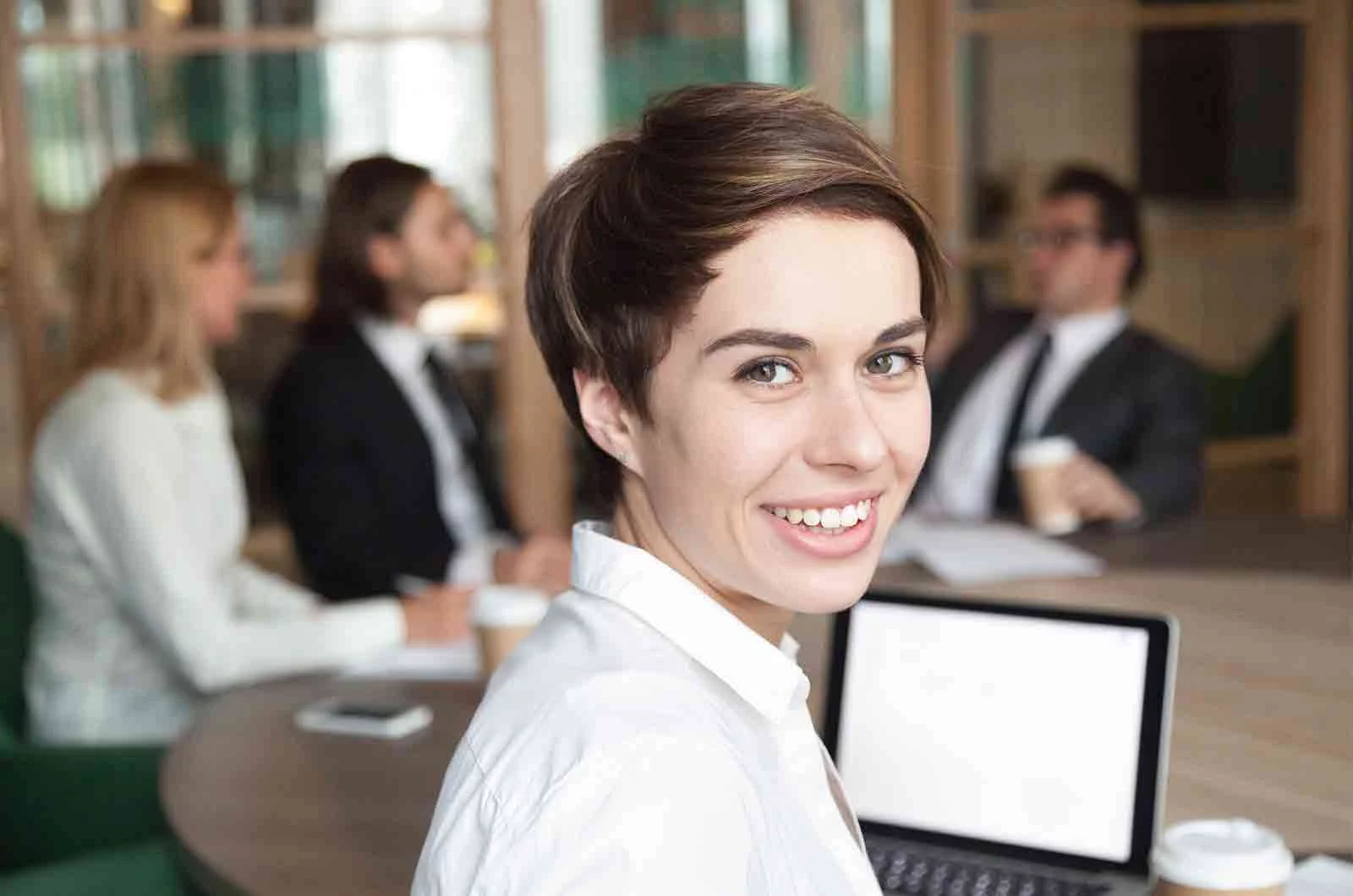 Brown-haired girl smiling with co-workers behind her at a business meeting. Concept of language translation services office.