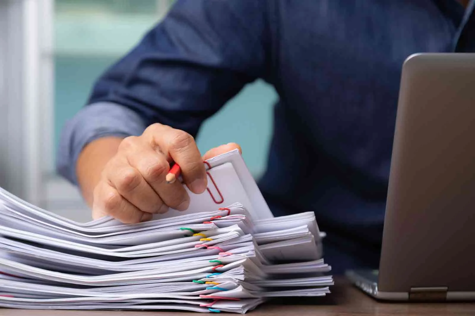 Man sitting on desk, holding a pencil, using a laptop and working on files. Concept of translating documents by a freelance translator or a translation company.