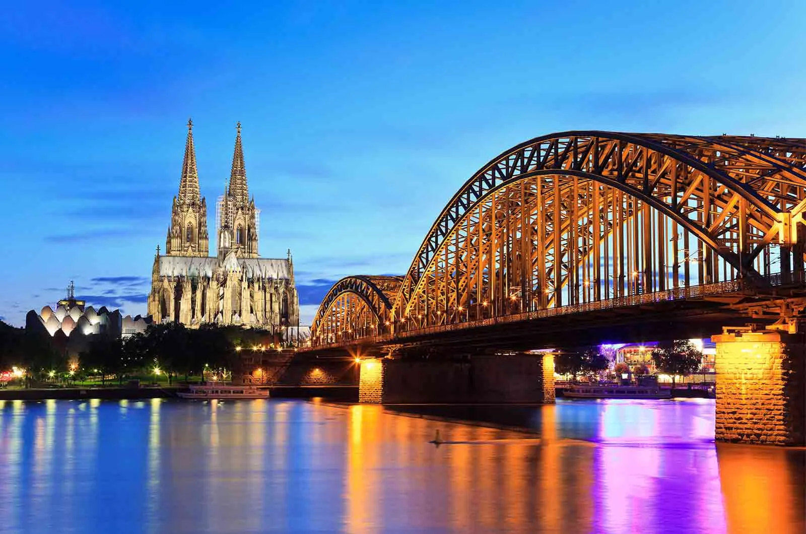 Night-time skyline of Cologne, Germany, with an iron bridge over a river. Concept of German translation services.
