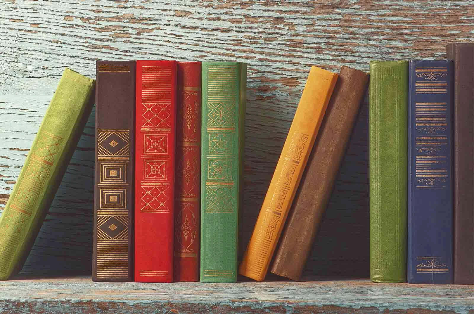 A group of old books with bold-coloured covers on a wooden shelf. Concept of translating books.