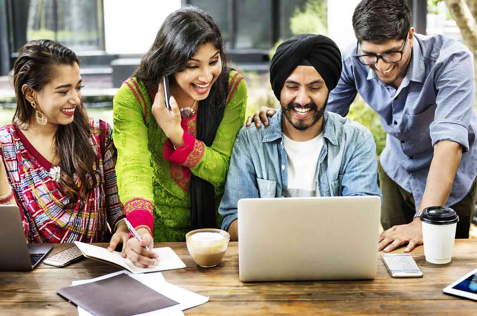 Two Indian women and two Indian men looking at their laptop. Concept of English to Hindi translation and Hindi translators.