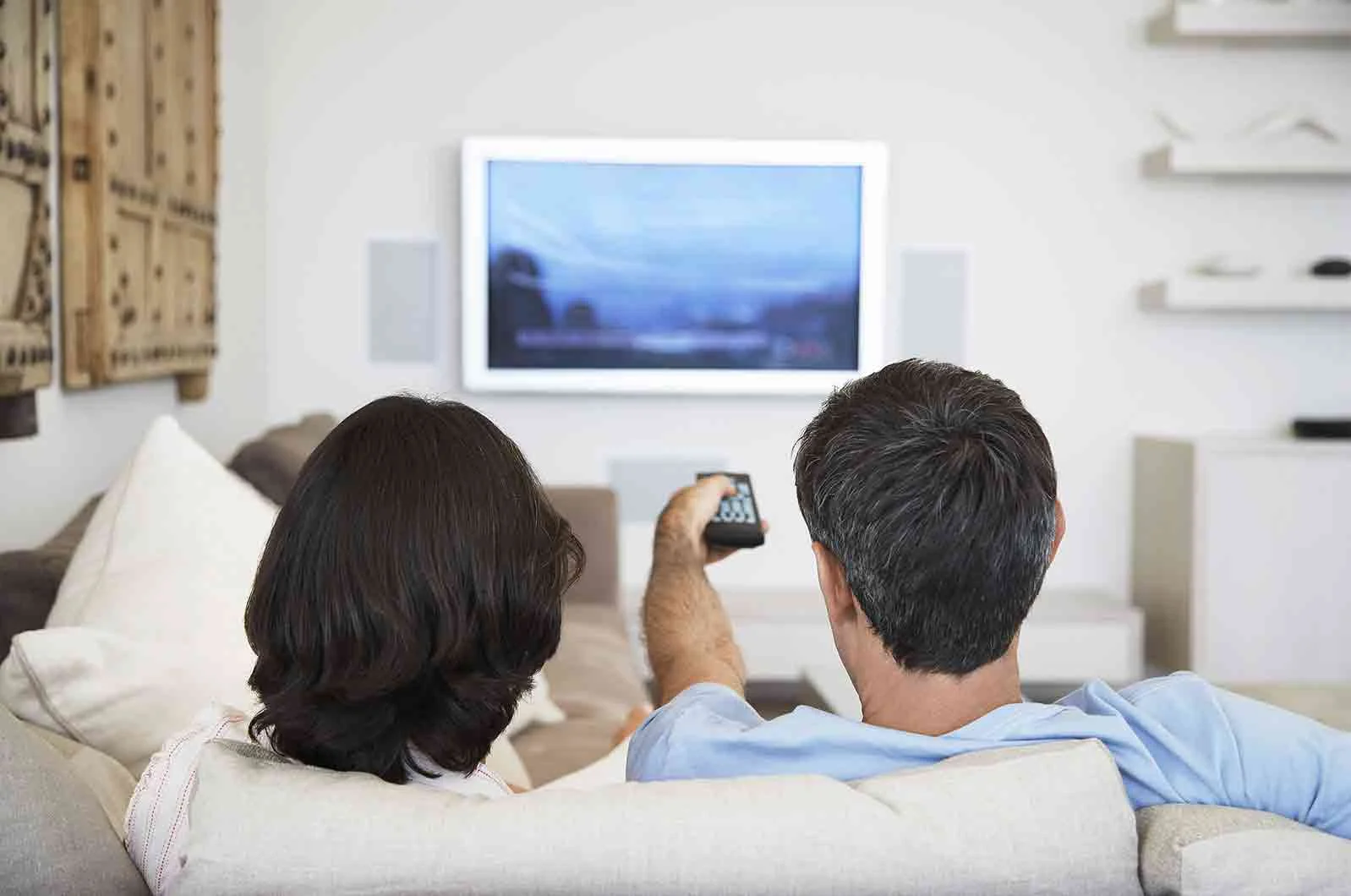 Couple watching TV, one of them holding the remote control. Concept of subtitling service.