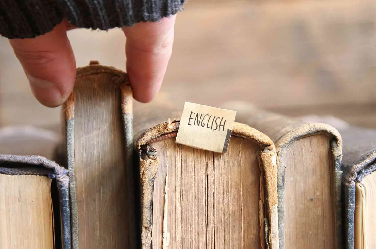 A group of old books, one labelled English, and someone choosing a book. Concept of translating to English.