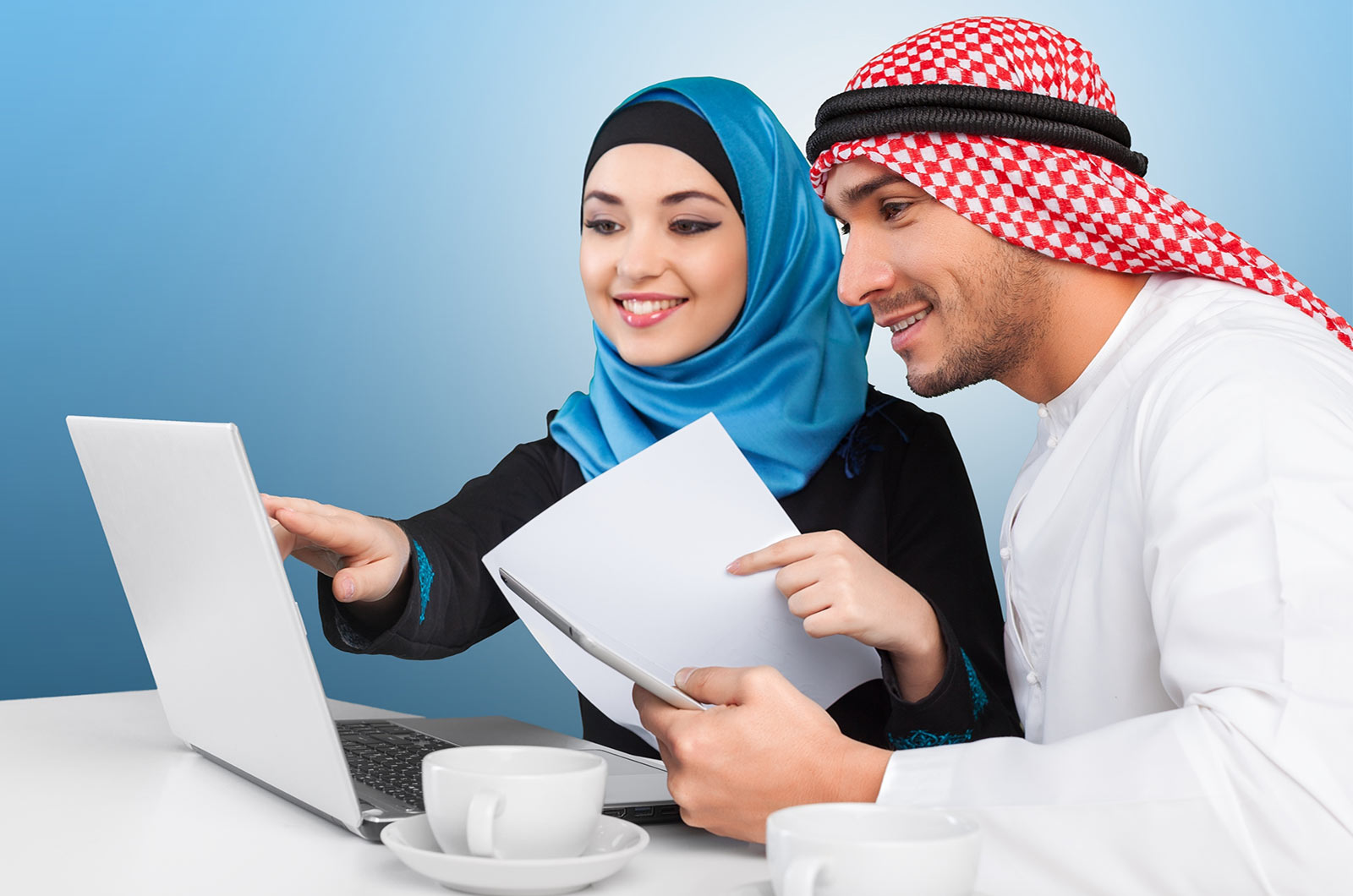 A girl wearing hijab and a man wearing traditional Arabic clothing, sitting on a desk with a laptop. Concept of English to Arabic translation.