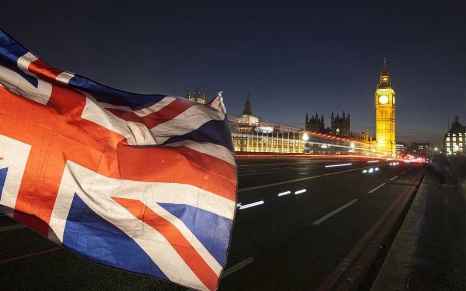 A night view of the union jack flag and the Big Ben in the background in London, UK. British accents and dialects in the UK.