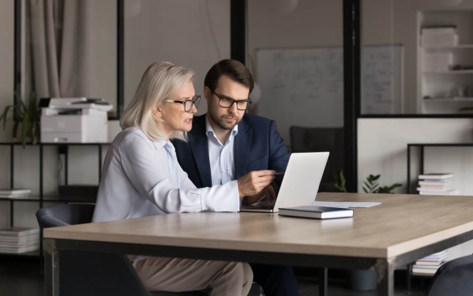 Two senior managers sitting at desk in office looking at computer screen, discussing development of multilingual websites for the business. 