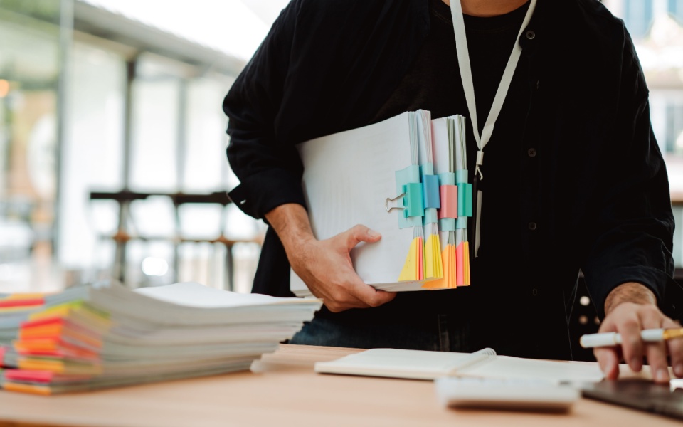 An employee preparing large number of documents for translation on a desk in an office.