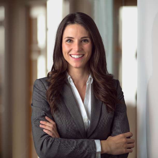 A professional smiling businesswoman standing in office with folded hands.