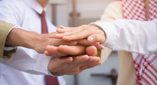 Arab businessman and other people putting their hands together expressing teamwork.