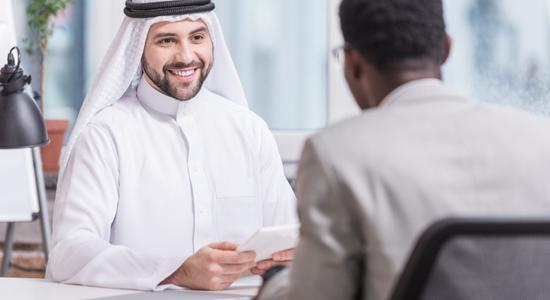 An Arabic man smiling at another Arabic man sitting in front of him.