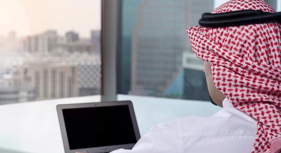 Arab man watching laptop in office. Concept of website translation to Arabic.