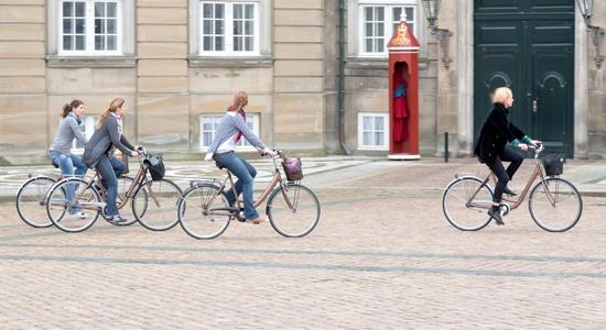 Three Danish women riding bicycles in town, Denmark. Concept of professional Danish translators.