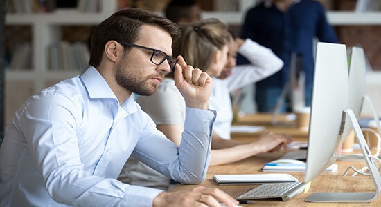 Confident and highly focused man with glasses working on computer.