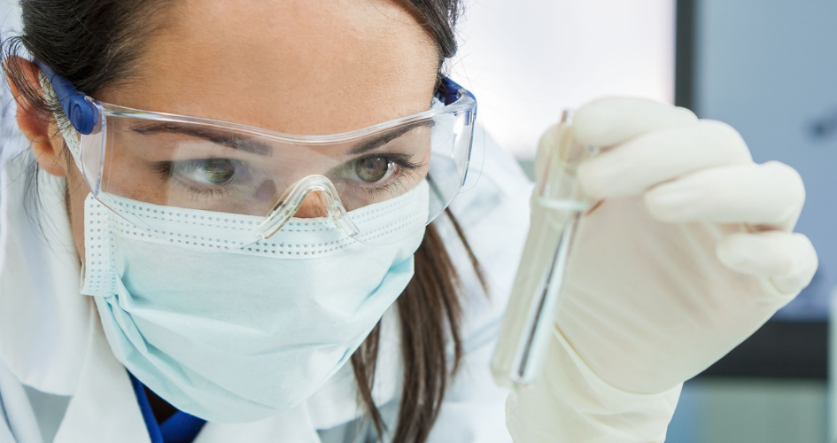 Close-up of a scientist in goggles and mask inspecting a test tube. Concept of chemistry translation, chemical translation and chemistry terms.