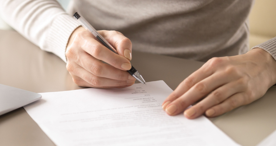 A person signing a contract on a desk with a black pen. Concept of contract translation by professional contract translators.