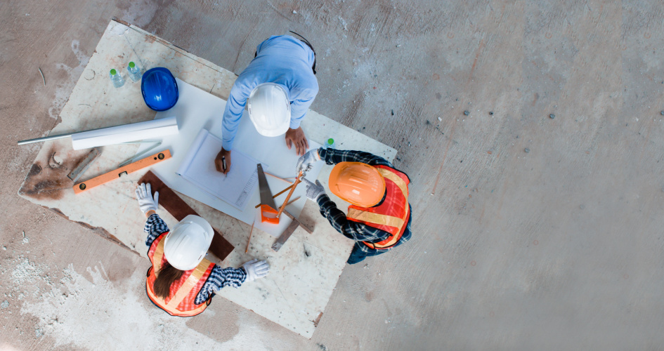 Overhead view of three construction workers designing at a worktable. Concept of construction translation services.
