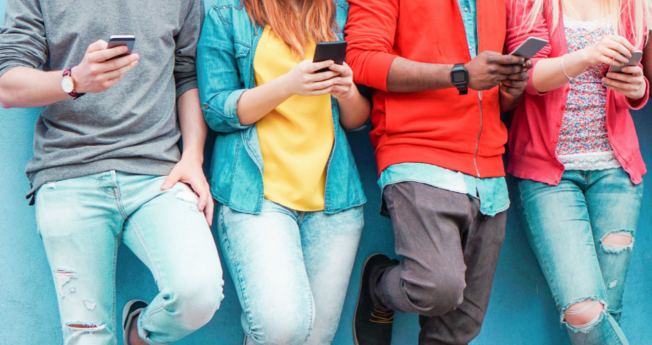 Close-up of 4 people in colourful clothes looking at their phones. Concept of app translation and app translators.