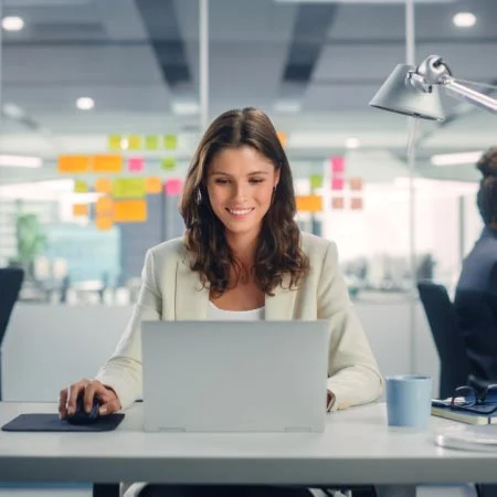 Professional young woman using computer in office with her colleagues in the background.