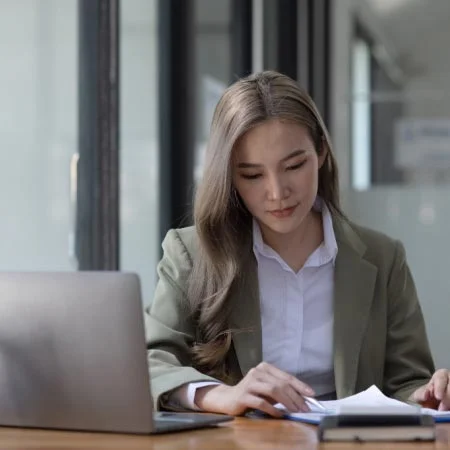 Asian professional woman wearing suit and working on laptop and papers. 