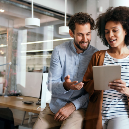 Two employees standing in corporate office discussing work progress on iPad.