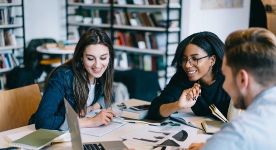 Two women and one man working using a laptop on a messy table. Concept of education translation.