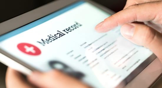 A person's hands holding a tablet looking at a medical record.