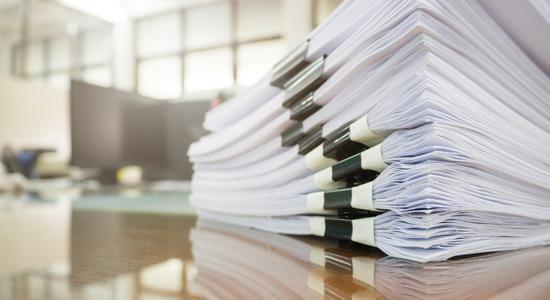 A stack of papers organized by binder clips, piled on a desk. 
