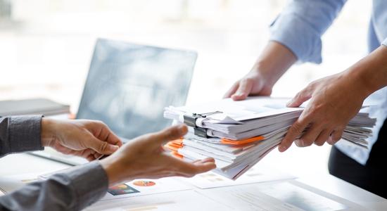 Businessman handing in stack of documents to an employee.