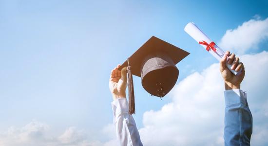 A blue sky and a student's hand holding a graduation cap.