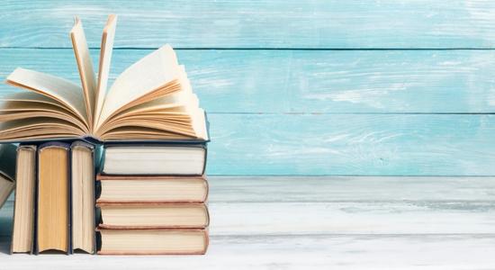 Several books stacked neatly in front of light blue wood surface. Concept of book translation services.
