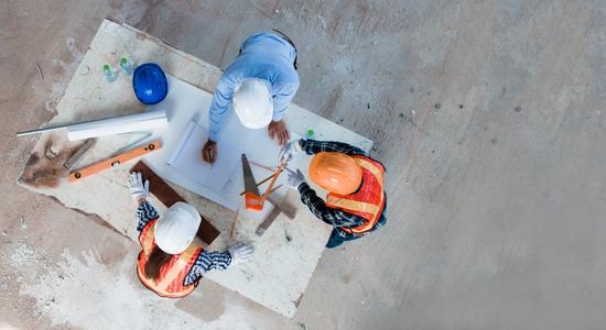 Overhead view of three construction workers designing at a worktable. Concept of construction translation services.