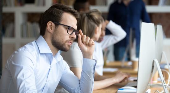 A man with glasses frowning at his computer monitor. Concept of insurance translator. 