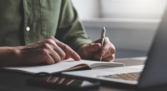 A man writing in a notebook with a laptop in front. Concept of book translators.