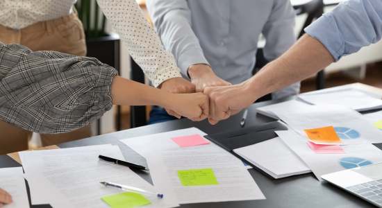 Team members joining fists over a table. Concept of proofreading company.