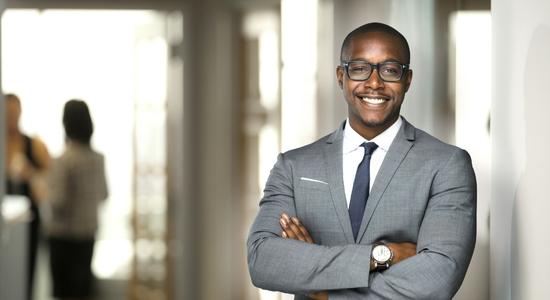 A bespectacled, dark-skinned businessman smiling at the camera. 