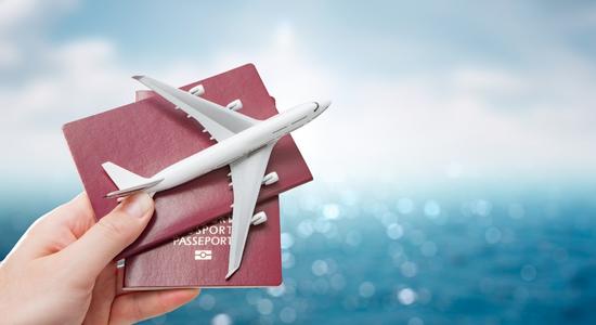 A hand holding two maroon passports and a model aeroplane.