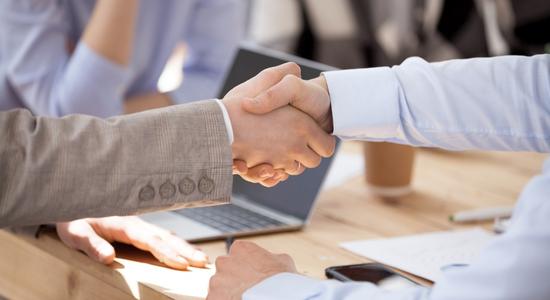 Two people shaking hands at a conference table.