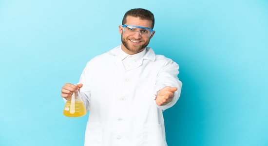 Smiling scientist holding chemical flask in one hand, other outstretched to camera. 