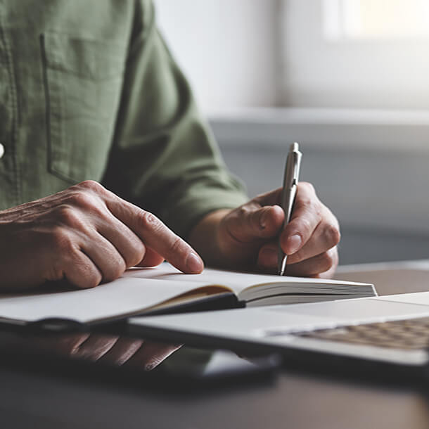 African man wearing suit and glasses smiling and signing paper.