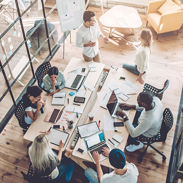 Two young employees celebrate success by giving high-five while their colleagues sitting and smiling.
