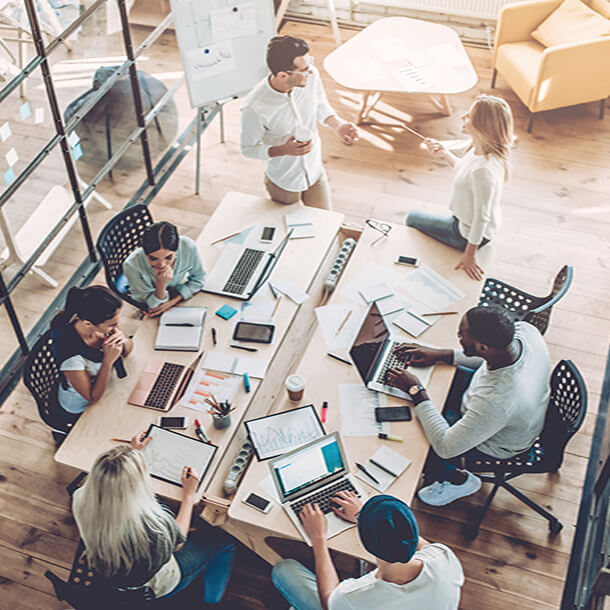 Two young employees celebrate success by giving high-five while their colleagues sitting and smiling.