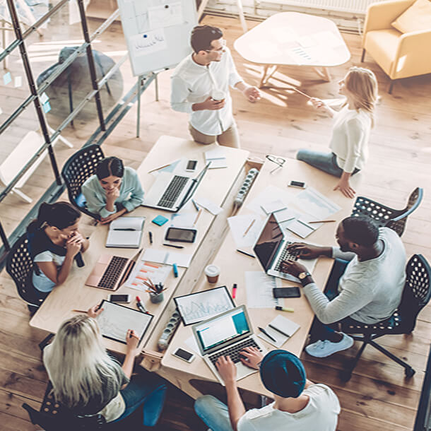 Two young employees celebrate success by giving high-five while their colleagues sitting and smiling.